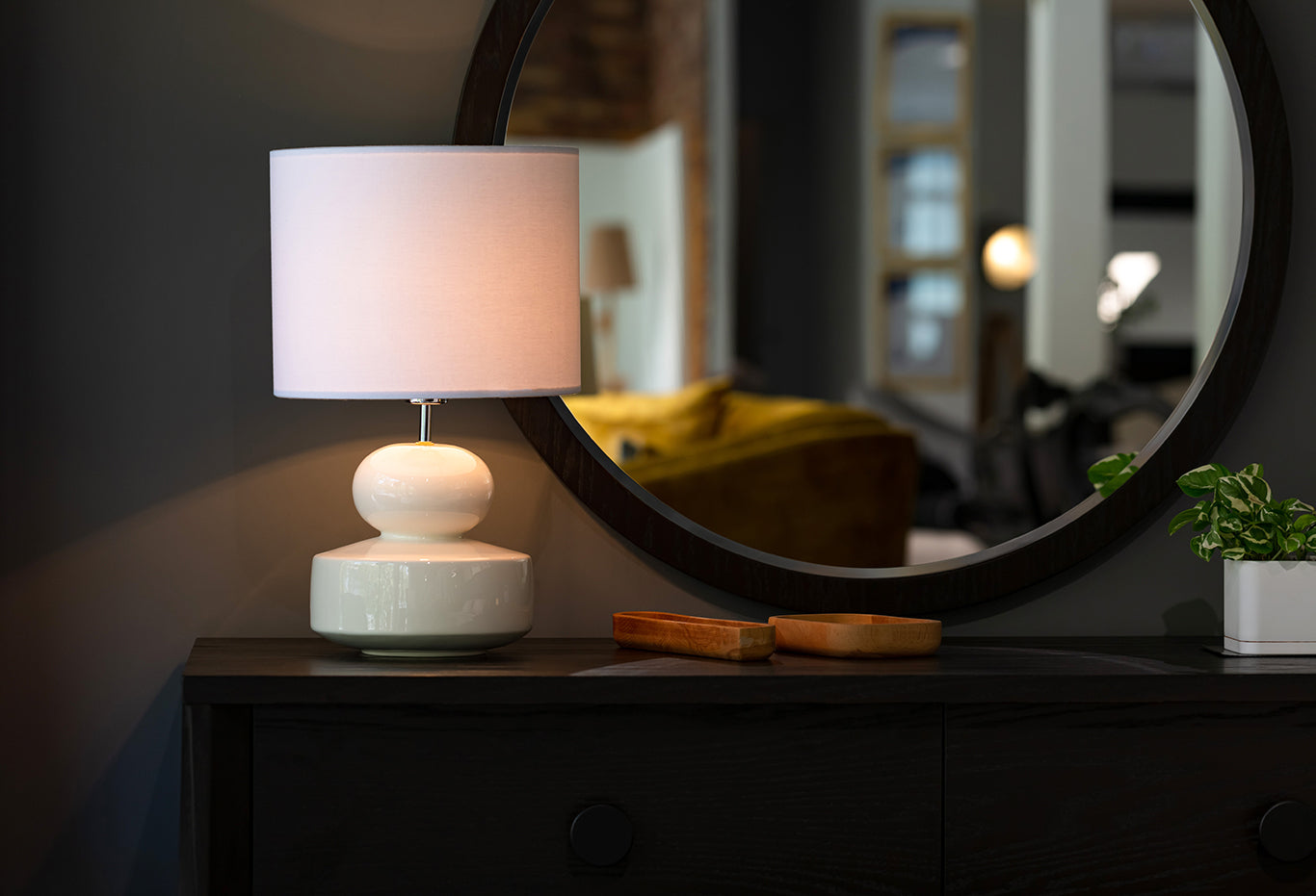 A table lamp and lampshade sitting on top of a dresser in front of a mirror