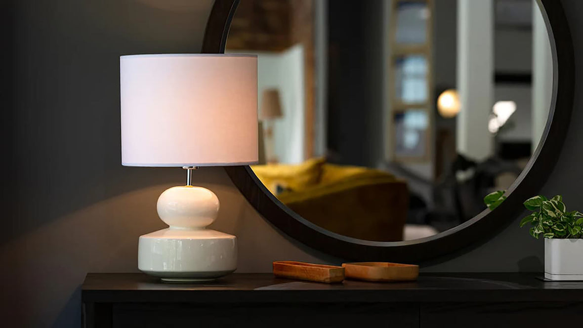 A table lamp and lampshade sitting on top of a dresser in front of a mirror