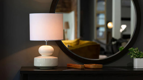 A table lamp and lampshade sitting on top of a dresser in front of a mirror
