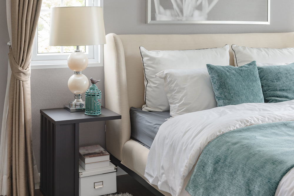 A pearl lamp and matching lamp shade sitting on a night table next to a bed in an elegant bedroom.