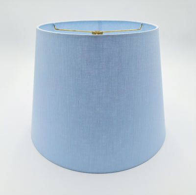 The Linen British Empire (Rolled Edges) is a light blue, hard-backed lampshade with a slightly tapered cylindrical shape, smooth fabric texture, and a gold metal fitting at the top, shown on a plain white background.
