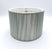 The String Short Drum is a cylindrical, light gray silk lampshade featuring a subtle vertical textured pattern and an internal gold metal frame, shown against a plain white background.