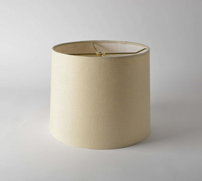 The Linen Short Drum (Rolled Edges) is a plain beige modern lamp shade with a cylindrical shape and a slightly wider bottom, displayed against a light gray background.