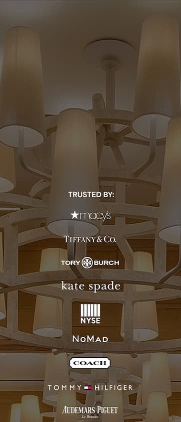 A chandelier with multiple lamps in the background. Overlaid text reads “Trusted by:” followed by logos for Macy’s, Tiffany & Co., Tory Burch, Kate Spade, NYSE, NoMad, Coach, Tommy Hilfiger, and Audemars Piguet.