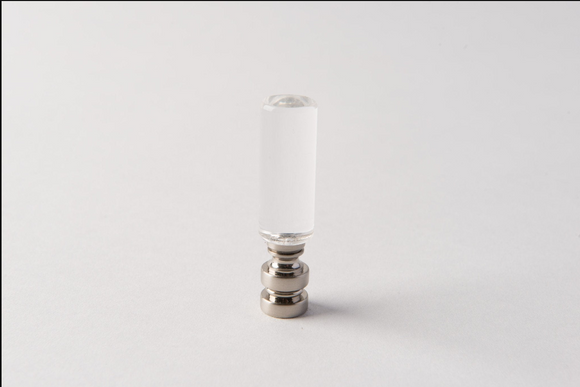 An Antique Brass Chinese Coin Finial stands upright on a plain white surface, centered in the image with a minimal background. The finial features a clear cylindrical glass body and a metallic antique brass base.