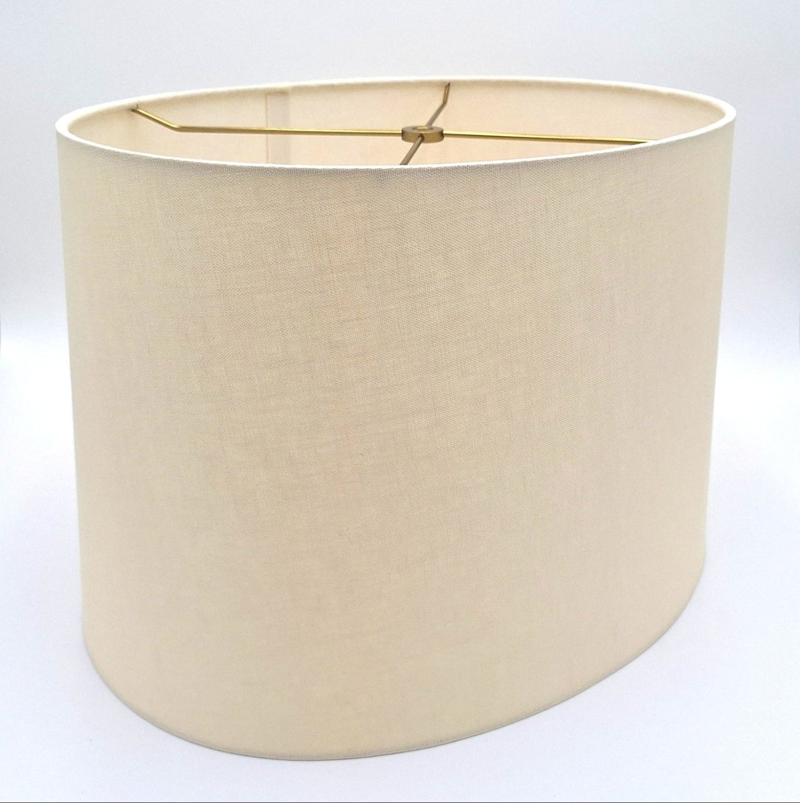 A tapered eggshell linen oval lampshade with rolled edges and brass spider hardware, shown against a plain white background.