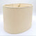 A tapered eggshell linen oval lampshade with rolled edges and brass spider hardware, shown against a plain white background.