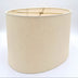 A tapered eggshell linen oval lampshade with rolled edges and brass spider hardware, shown against a plain white background.