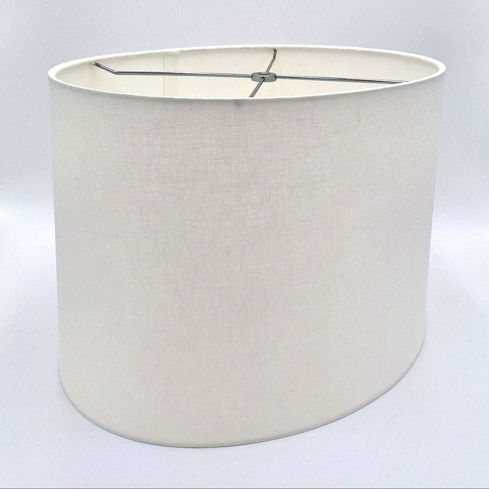 A tapered bone linen oval lampshade with rolled edges and nickel silver spider hardware, shown against a plain white background.