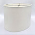 A tapered bone linen oval lampshade with rolled edges and nickel silver spider hardware, shown against a plain white background.
