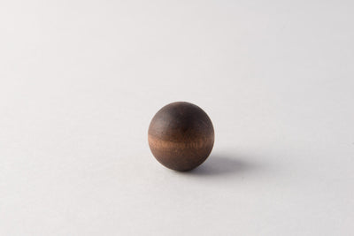 The Wood Ball Finial, crafted from dark wood, sits on a light surface with a gentle shadow to the right, highlighting its minimalist design.
